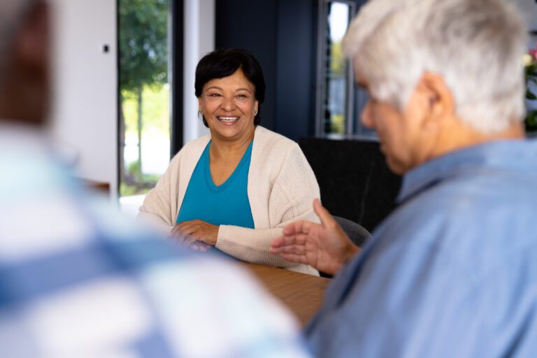 Smiling biracial senior woman talking with male friend while sitting at dining table in nursing home. Lunchtime, unaltered, friendship, togetherness, support, assisted living and retirement concept Image description